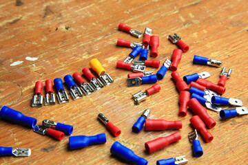 Verstreute rote und blaue isolierte Crimp- und Flachstecker mit sichtbaren Metallkontakten auf Holz; typische Komponenten f&uuml;r KFZ-, Elektrik- und Heimwerkerarbeiten.