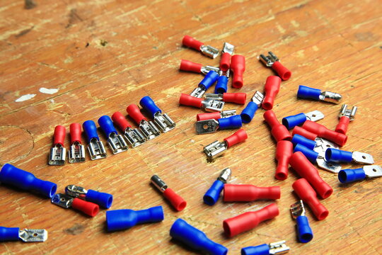 Verstreute rote und blaue isolierte Crimp- und Flachstecker mit sichtbaren Metallkontakten auf Holz; typische Komponenten f&uuml;r KFZ-, Elektrik- und Heimwerkerarbeiten.
