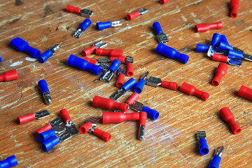 Verstreute rote und blaue isolierte Crimp- und Flachstecker mit sichtbaren Metallkontakten auf Holz; typische Komponenten f&uuml;r KFZ-, Elektrik- und Heimwerkerarbeiten.