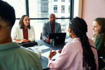 Confident young businesswoman sharing ideas during team meeting in office boardroom at daytime