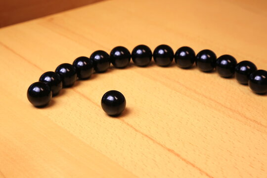 Schwarze, gl&auml;nzende Kugeln auf hellem Holz bilden eine Reihe mit einer herausgehobenen, vorderen Kugel. Minimalistisch, kontrastreich, symbolisch f&uuml;r Individualit&auml;t und F&uuml;hrung.
