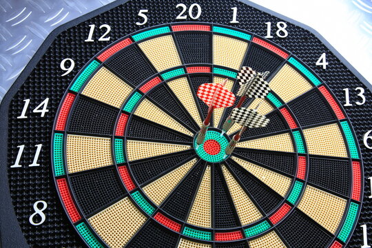 Drei Dartpfeile stecken pr&auml;zise in der Dartscheibe. Die kr&auml;ftigen Farben und der metallische Hintergrund betonen den Moment sportlicher Konzentration.