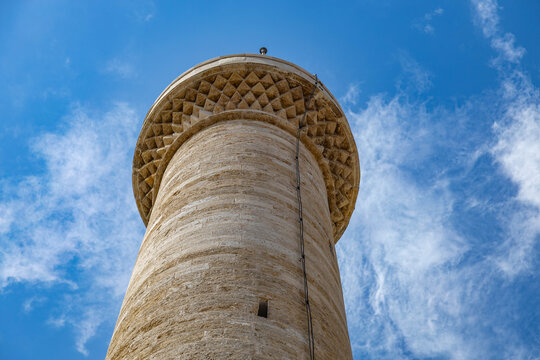 Low-angle view of a historic minaret with intricate stone mukarnas carving on its balcony, reaching into a blue sky with white clouds. e.  Mediterranean, Kaleici, Antalya, Turkey