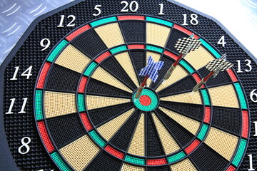 Drei Dartpfeile stecken pr&auml;zise in der Dartscheibe. Die kr&auml;ftigen Farben und der metallische Hintergrund betonen den Moment sportlicher Konzentration.