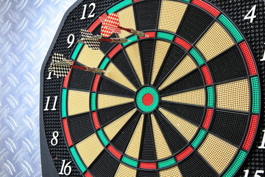 Drei Dartpfeile stecken pr&auml;zise in der Dartscheibe. Die kr&auml;ftigen Farben und der metallische Hintergrund betonen den Moment sportlicher Konzentration.