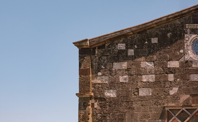 Detailed view of the rugged eastern historical church stone wall featuring intricate carvings and an artistic circular frame against a clear blue sky. Ideal background for tourism.