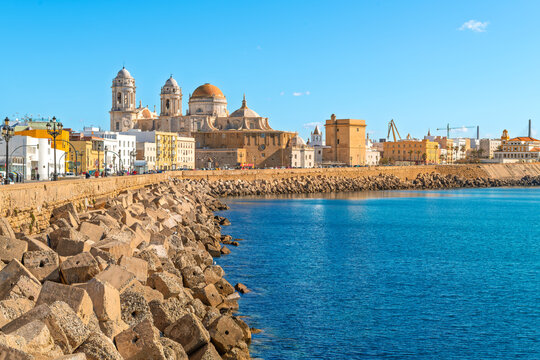 View from the rocky coastline of Paseo del Vendaval Promenade at Campo del Sur of historic Cadiz Cathedral, or Catedral de la Santa Cruz de C&aacute;diz, in Cadiz Spain. 