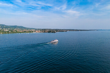 Obraz premium Passenger ferry crossing Lake Garda between towns, aerial. Public transport service providing intertown lake transit on a scheduled route