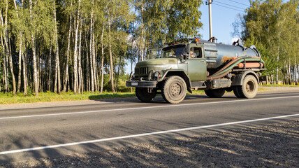 Retro tanker truck travels along an asphalt road through the forest. Delivering fuel for agricultural machinery during the harvest.