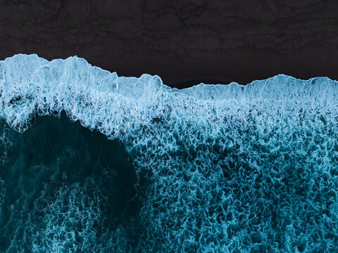 Strong waves of ocean reaching black sandy beach at sunrise. Aerial Volcanic beach or coastline of Azores