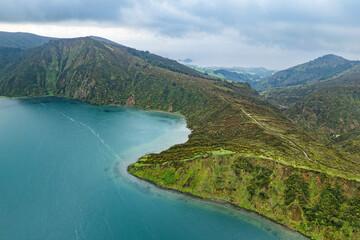 Natural caldera lake surrounded by volcanic mountains and forested slopes, low clouds moving across the landscape. Lagoa do Fogo, Sao Miguel island, Azores, drone view