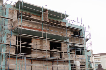 Construction continues on a multi-story building with scaffolding around the structure. Workers are present, and the building is in an urban area near other buildings