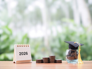 Study goals, 2026 Desk calendar, Glass bottle with graduation hat and stack of coins. The concept of saving money for education, student loan, scholarship, tuition fees in year 2026