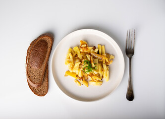 Fried potatoes with green onions on a round plate, rye bread and a fork on the table, top view