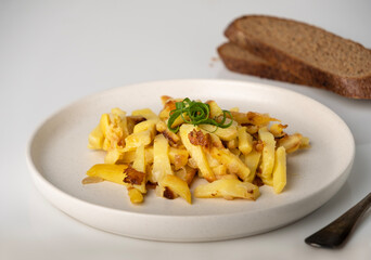 Fried potatoes with green onions on a round plate on the table