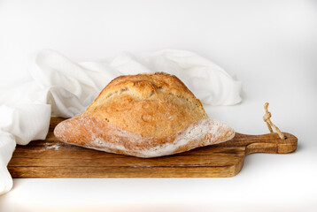 Homemade bread lies on a wooden board with white cloth, side view, space for text.