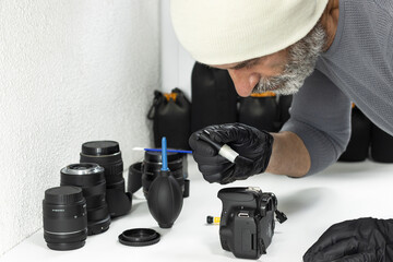 Professional photographer carefully cleaning a digital camera and lenses with brush and air blower, camera maintenance, photography equipment care, studio workspace.