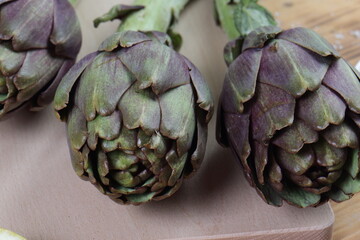 Obraz premium Raw Purple Artichokes on Cutting Board with Mediterranean Ingredients: Lemon, Garlic, and Olive Oil