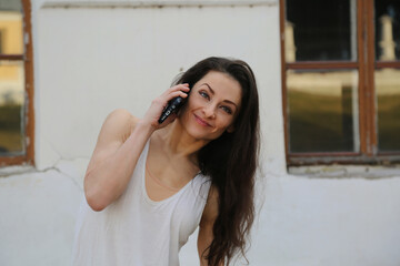 Beauty emotion face fit woman happy talking on mobile phone in white dress, long brown hair. Closeup relaxing emotional face portrait outdoors on summer houses background