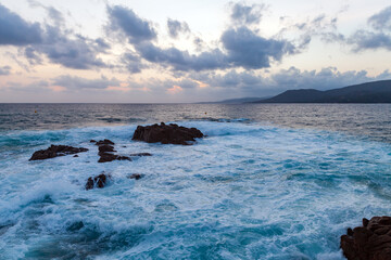 Black rocks are in shore waters at sunset. Coastal landscape of Propriano, Corsica