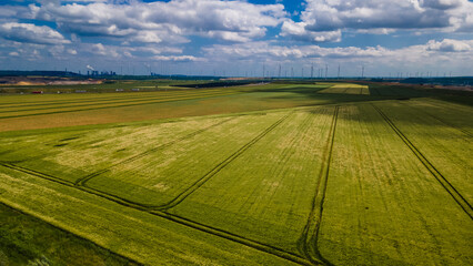 Scenic industrial landscape showing the contrast between traditional agriculture and modern energy production with wind farms and a thermal power station under a summer sky