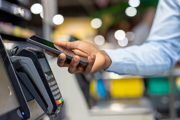Person making a digital transaction using a mobile phone at a checkout counter, showing modern nfc technology for seamless cashless payment in a retail environment