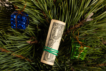A rolled-up one-dollar bill on the branches of a Christmas tree with small gifts in colorful packaging, a symbol of a monetary gift, profit, prosperity
