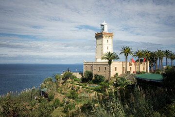 Cape Spartel Lighthouse overlooking the Atlantic near Tangier, surrounded by palm trees and gardens, where the ocean meets the Strait of Gibraltar under a bright sky.