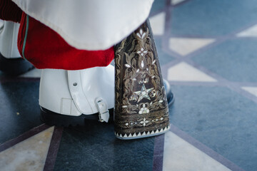 Close-up of an ornate rifle butt beside polished boots, suggesting a ceremonial guard on duty. Traditional craftsmanship, formal stance, and symbolic military detail in a public space.