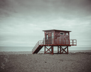  Minimalist shot of a lonely lifeguard tower on a deserted pebble beach under a dramatic cloudy sky.