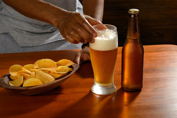 A man enjoying a cold beer with crispy french fries at a wooden table.