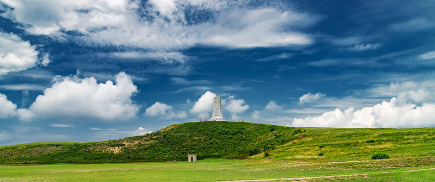 Wright Brothers National Memorial on grassy hill under dramatic blue sky