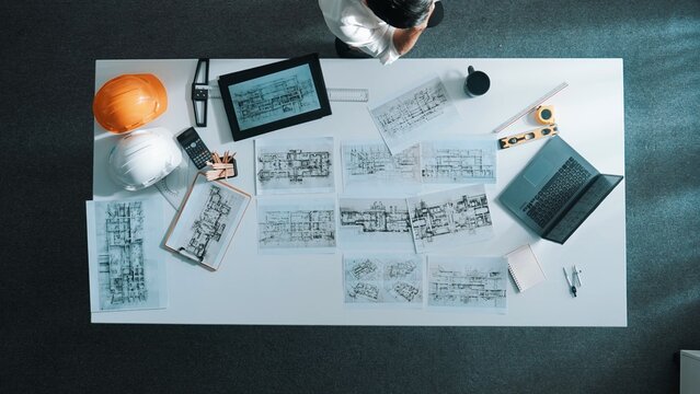 Time lapse of smart engineer looking at tablet while using laptop to analysis building structure. Aerial view of architect checking at interior design at meeting table with project plan. Alimentation.