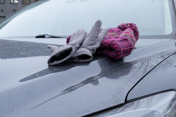 Pair of warm gloves and knitted scarf lying on car hood