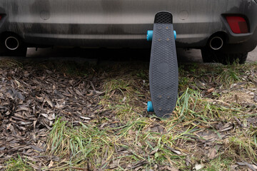 skateboard left standing near rear of parked car on rough ground