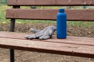 Pair of grey winter gloves and a bright blue reusable bottle lying on a wooden park bench