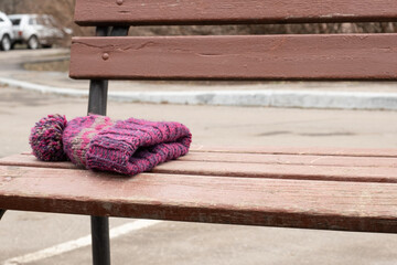 knitted winter hat with pom-pom lying alone on a wooden park bench