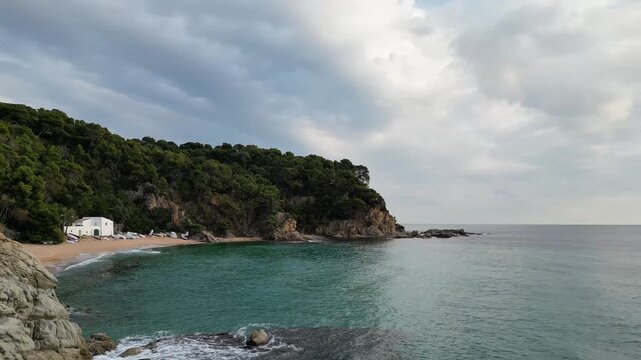 Aerial drone view, flying at the Spanish coastline with empty beach, mountains, blue sea and sky with clouds, Lloret de Mar, 4k nature background	