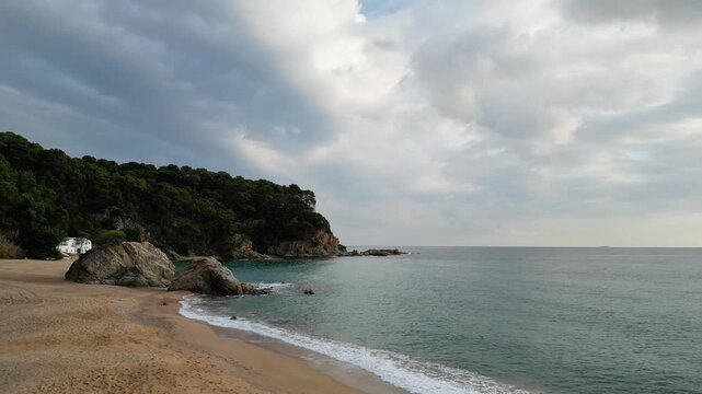 Aerial drone view, flying at the Spanish coastline with empty beach, mountains, blue sea and sky with clouds, Lloret de Mar, 4k nature background	