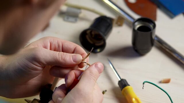 Craftsman working on transforming by-product into high quality upcycled item, man carefully removes old winding on wires and tightens exposed contacts with pliers tool. Renovation of old vintage lamp.