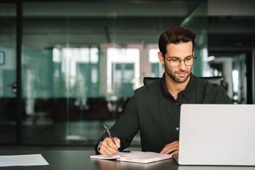 Middle-age European man using laptop computer for business studying, watching virtual webinar training writing notes. Focused young Latin businessman student working in office online, copy space © Stock 4 You