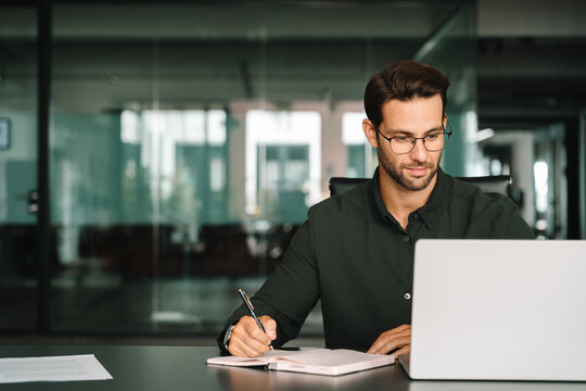 Middle-age European man using laptop computer for business studying, watching virtual webinar training writing notes. Focused young Latin businessman student working in office online, copy space