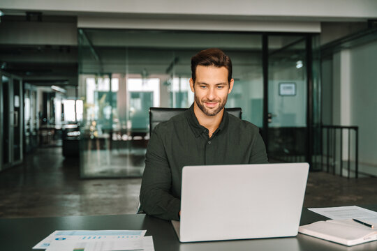 Young professional specialist latin hispanic businessman working on laptop pc sitting at desk in office. European businessman ceo specialist using computer technology app for work online. Copy space