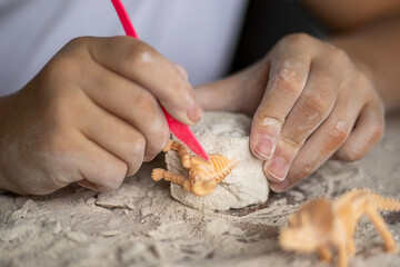 Child shaping dough with pink tool, sculpting a small orange dinosaur in a floury block © Nataliia