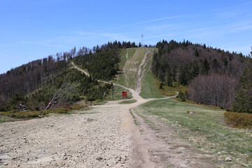 Wide view of Klimczok peak and mountain landscape with dirt road and hiking trail on green hillside in Beskid mountains