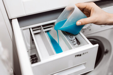 Hand pouring blue liquid detergent into washing machine drawer, showcasing laundry preparation...