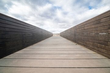 Fototapeta premium Empty wooden walkway under a cloudy sky with a stone wall in the background.