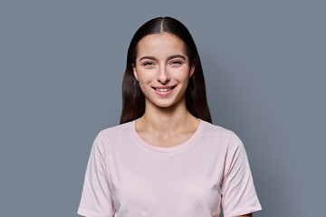 Fototapeta premium Portrait of beautiful smiling teenage girl against gray studio background