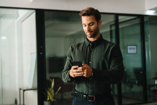 Mann ceo manager using digital technology cellphone phone mobile trade for business work online. Young Latin businessman holding smartphone telephone device standing in company office. Copy space