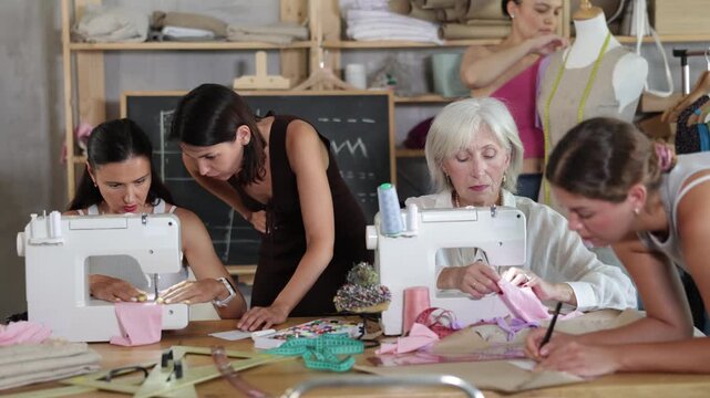 Group of women sew, draw pattern on paper and work with mannequin at sewing workshop 